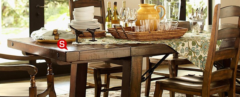 Ein stilvolles Esszimmer im Landhausstil mit einem Esstisch und Stühlen aus Massivholz. Auf dem Tisch stehen Geschirr und schwarze Dekorelemente.