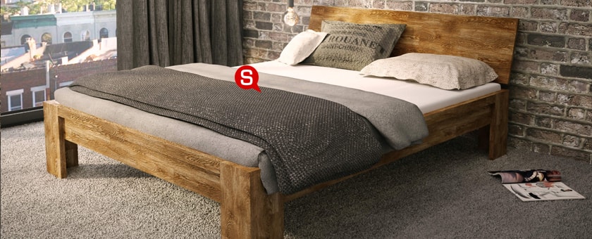 Ein minimalistisches Schlafzimmer mit einem großen Bett und Ziegelwänden. Unter dem Bett liegt ein beiger Kuschelteppich. Das Bett ist mit grauen Plaids bedeckt. 