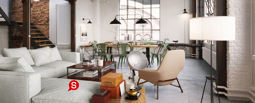 Eine industrielle Einrichtung mit einem grauen Sofa und einem Couchtisch aus Holz, gleich daneben steht ein beiger Sessel. Im Hintergrund sind ein Holztisch, Metallstühle und Hängelampen zu sehen.
